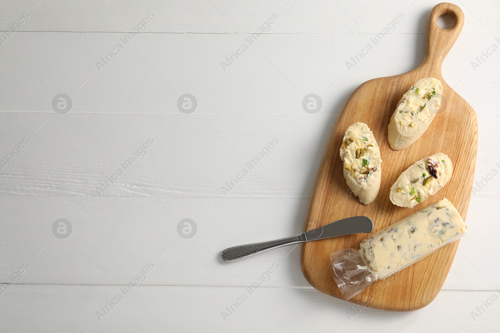 Photo of Tasty butter with green onion, olives and knife on white wooden table, top view. Space for text