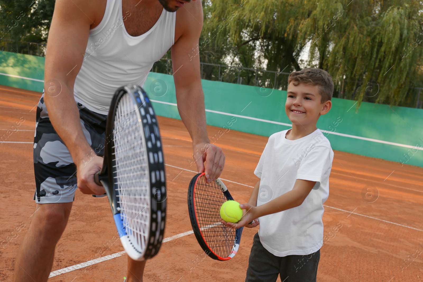 Photo of Father teaching son to play tennis on court