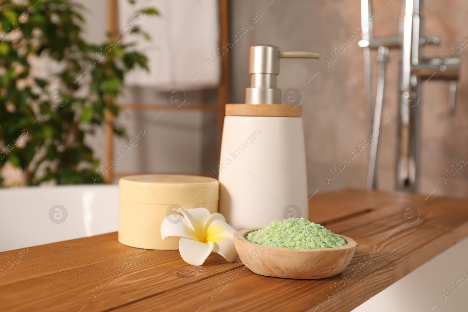 Photo of Spa products and beautiful plumeria flower on wooden tub tray in bathroom