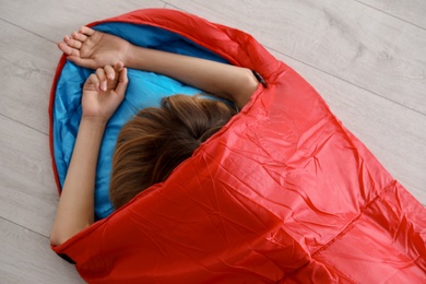 Photo of Young woman in comfortable sleeping bag on floor, top view