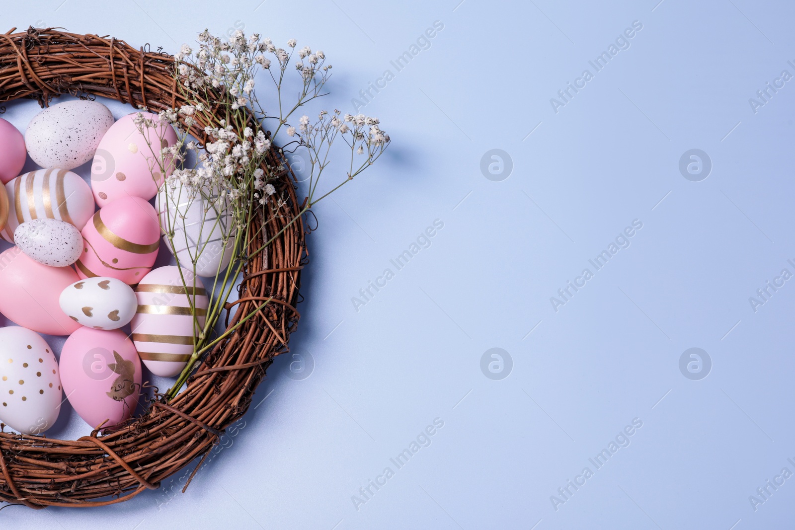 Photo of Festively decorated Easter eggs, vine wreath and gypsophila flowers on light blue background, top view. Space for text