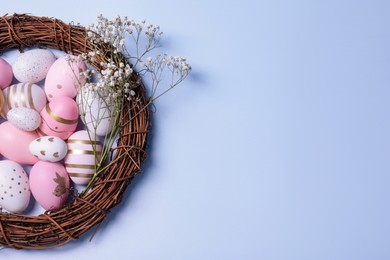 Festively decorated Easter eggs, vine wreath and gypsophila flowers on light blue background, top view. Space for text