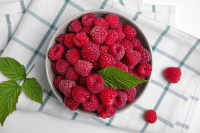Photo of Bowl with fresh ripe raspberries and green leaves on white table, flat lay