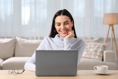 Photo of Happy woman working with laptop at wooden desk in room