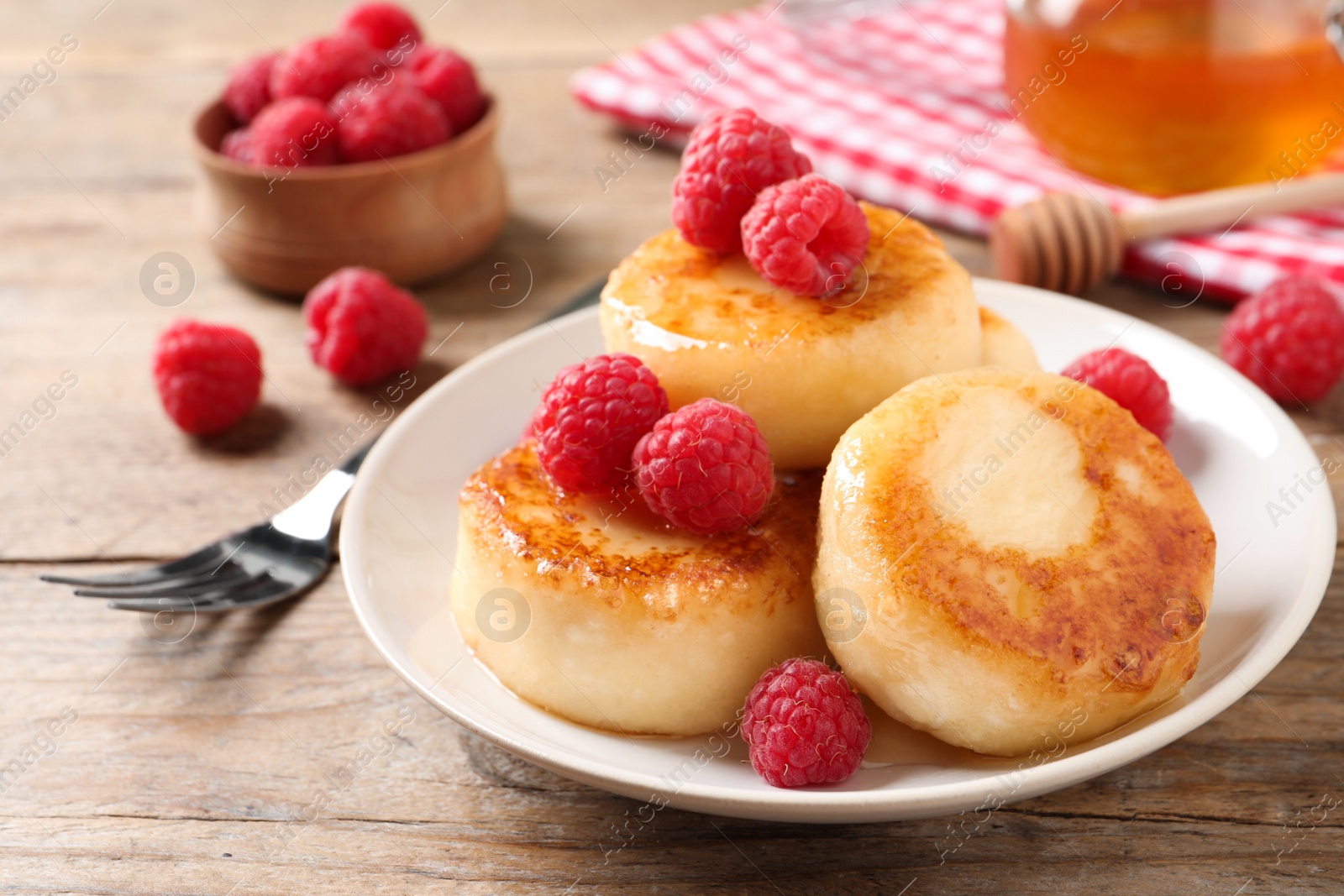 Photo of Delicious cottage cheese pancakes with raspberries on wooden table, closeup