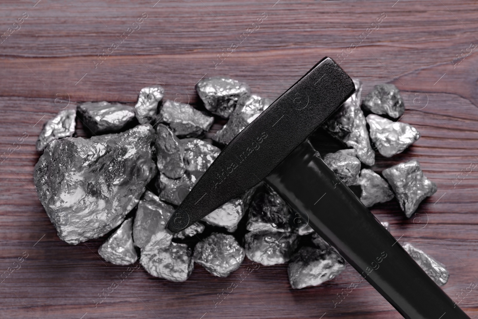 Photo of Pile of silver nuggets and hammer on wooden table, top view