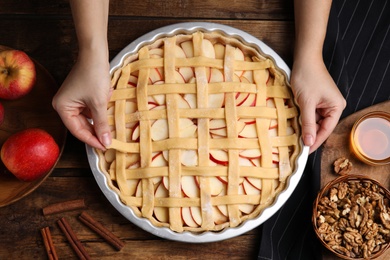 Photo of Woman making lattice top for traditional English apple pie at wooden table, top view