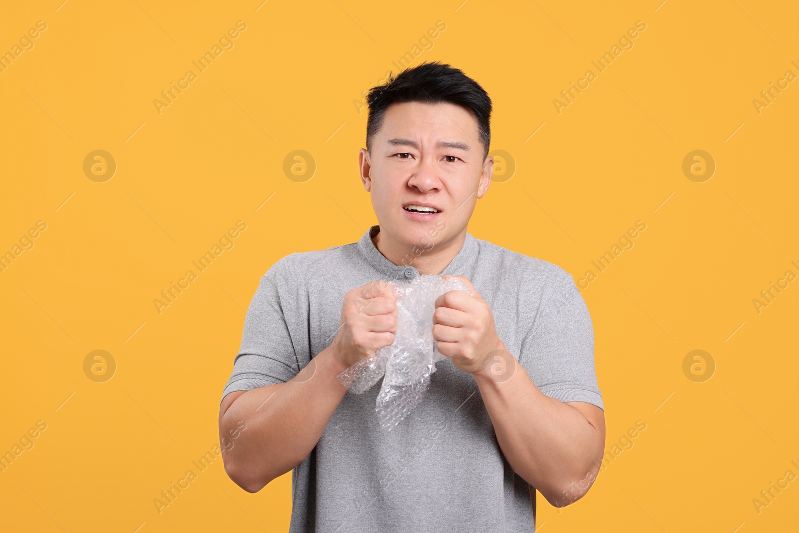 Photo of Emotional asian man with bubble wrap on orange background