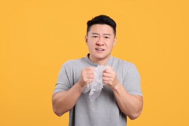 Emotional asian man with bubble wrap on orange background
