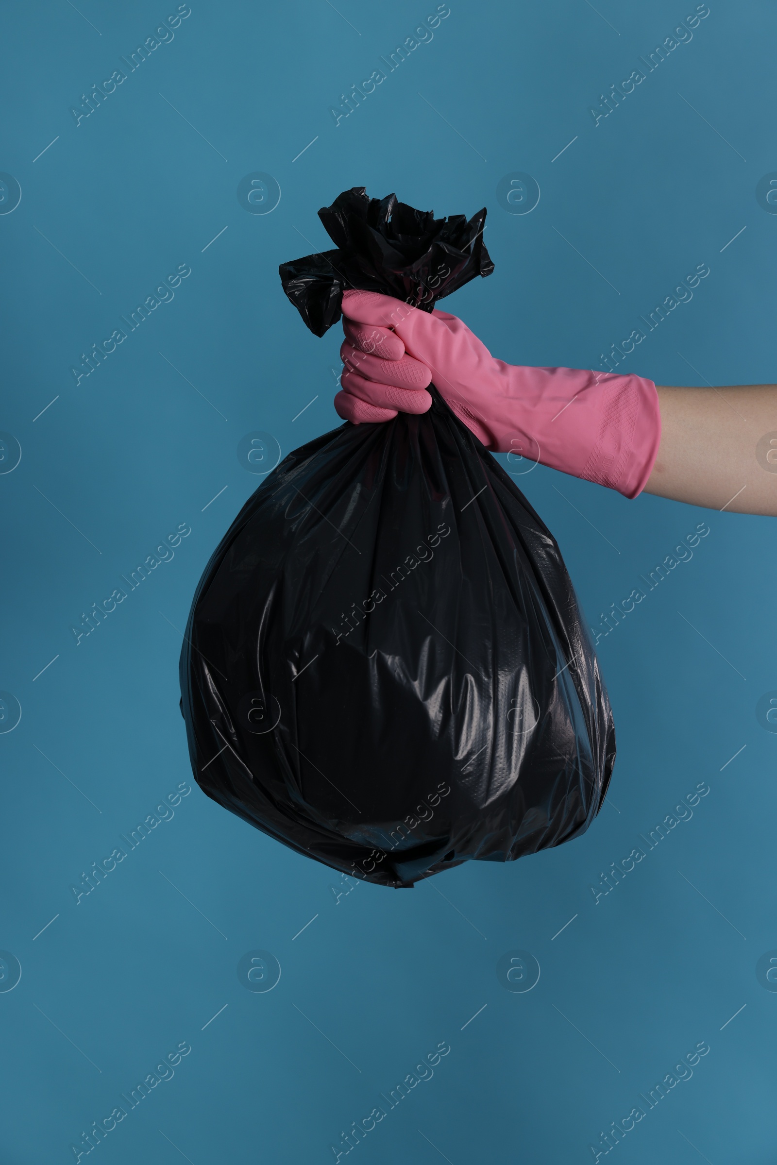 Photo of Woman holding plastic bag full of garbage on light blue background, closeup