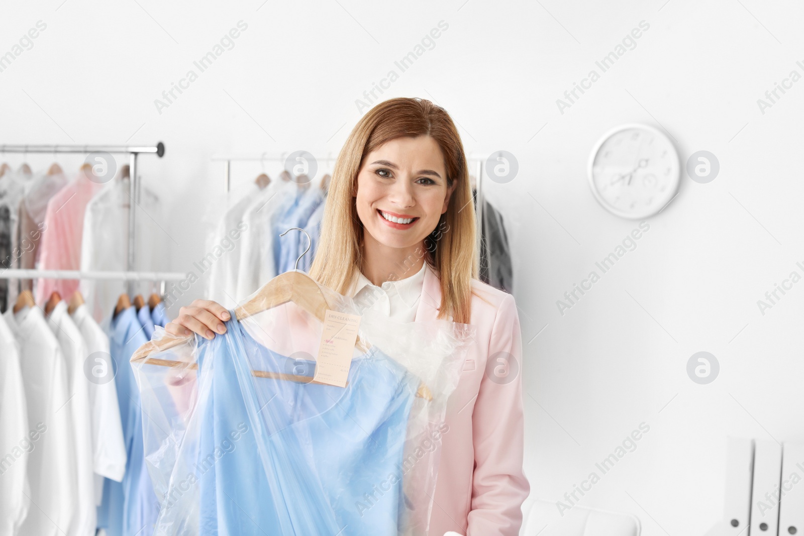 Photo of Young woman holding hanger with dress in plastic bag at dry-cleaner's