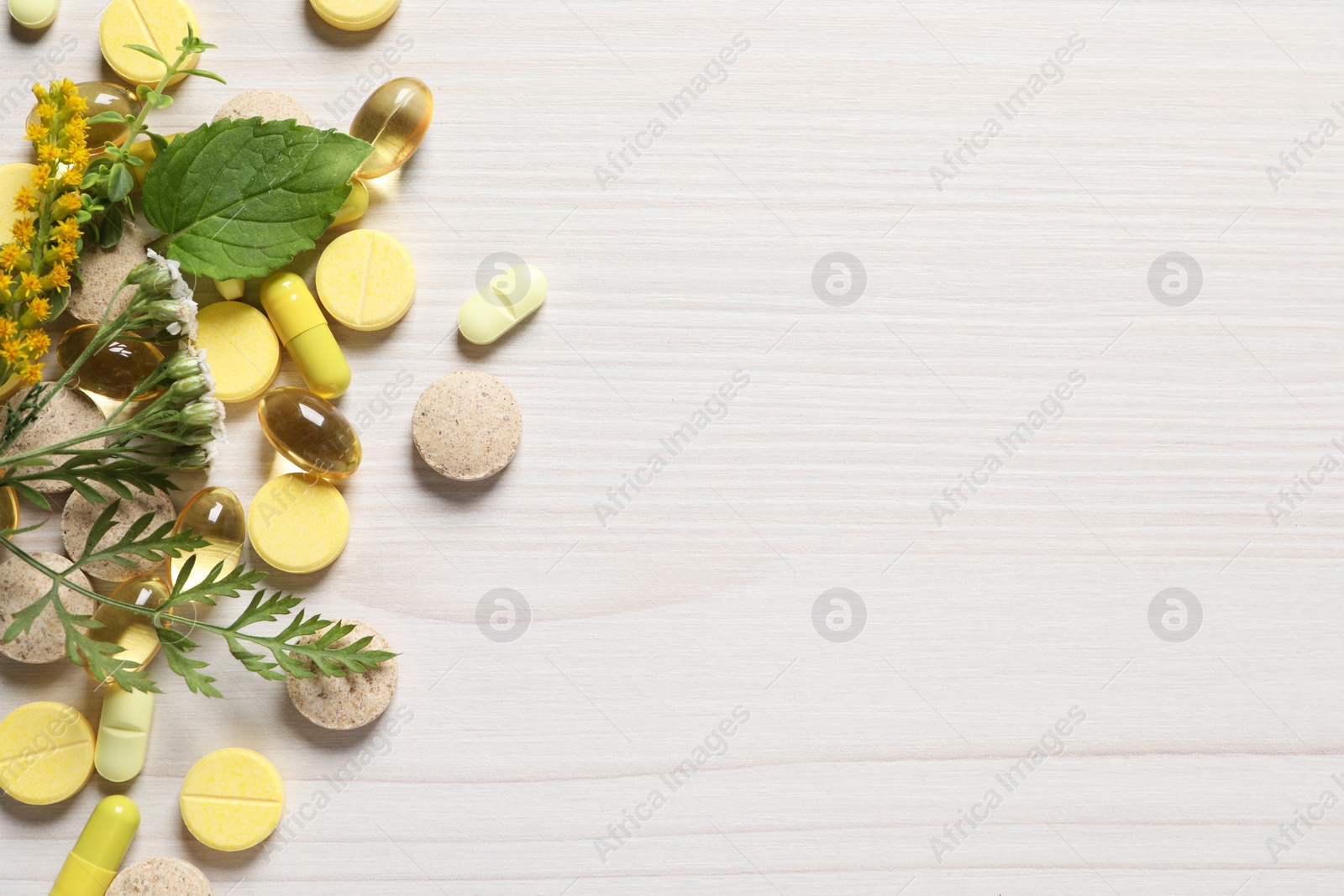 Photo of Different pills, herbs and flowers on white wooden table, flat lay with space for text. Dietary supplements