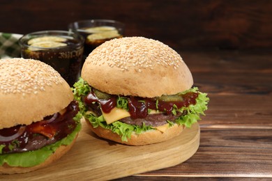 Board with delicious cheeseburgers on wooden table, closeup