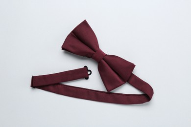 Stylish burgundy bow tie on white background, top view