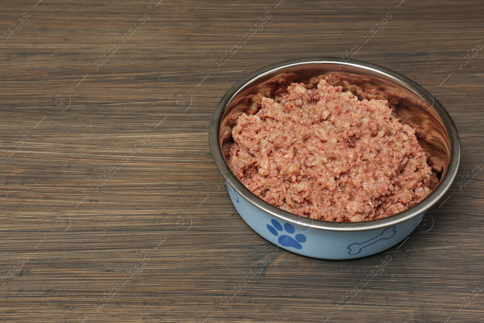 Photo of Wet pet food in feeding bowl on wooden background, space for text