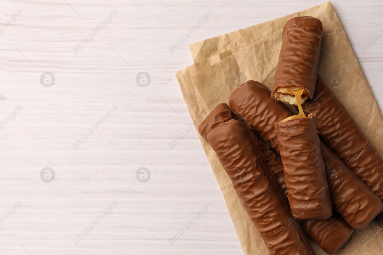 Photo of Tasty chocolate bars with caramel on white wooden table, top view. Space for text