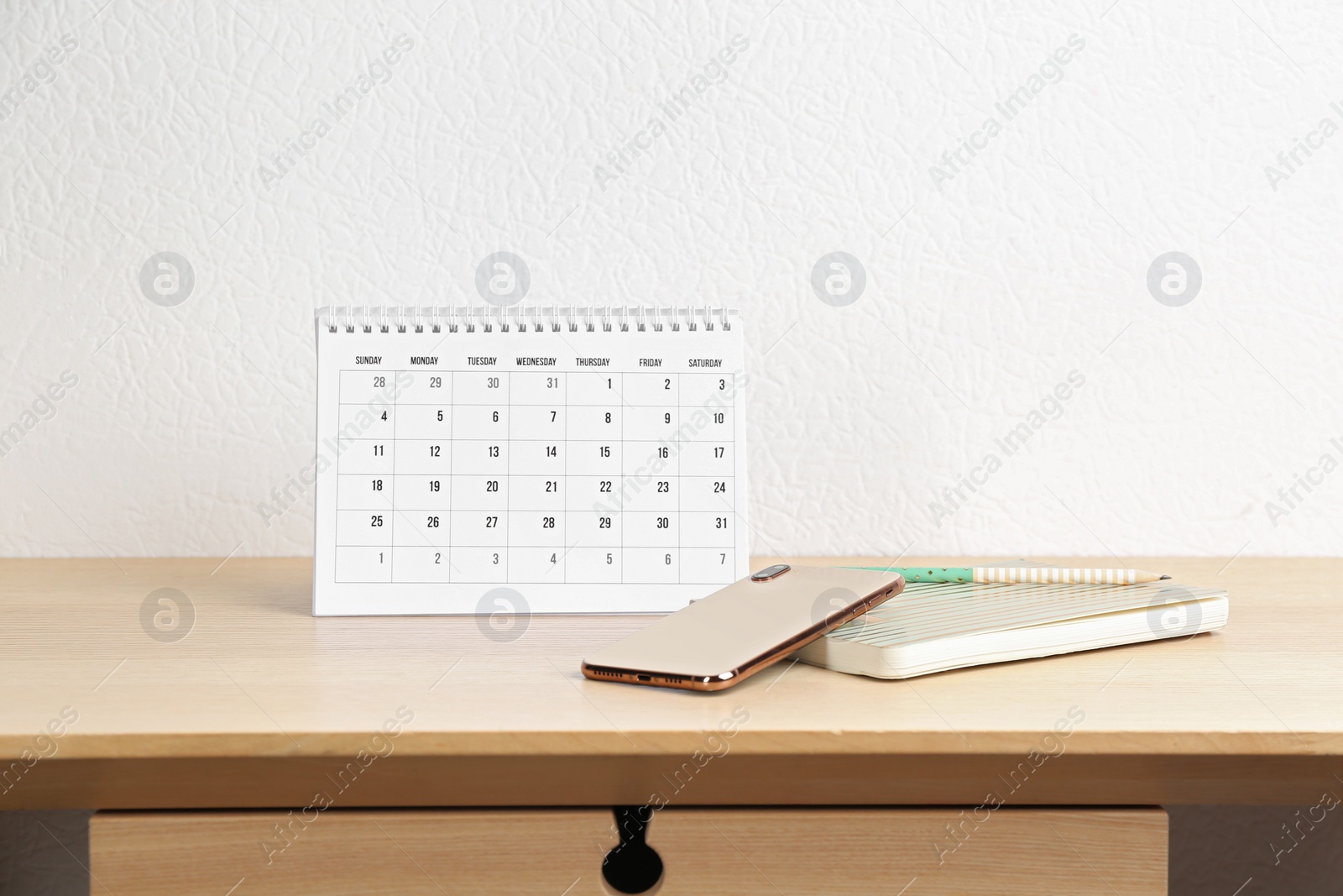 Photo of Paper calendar and smartphone on wooden table near white wall