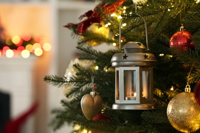 Christmas lantern with burning candle and balls on fir tree indoors, closeup. Space for text