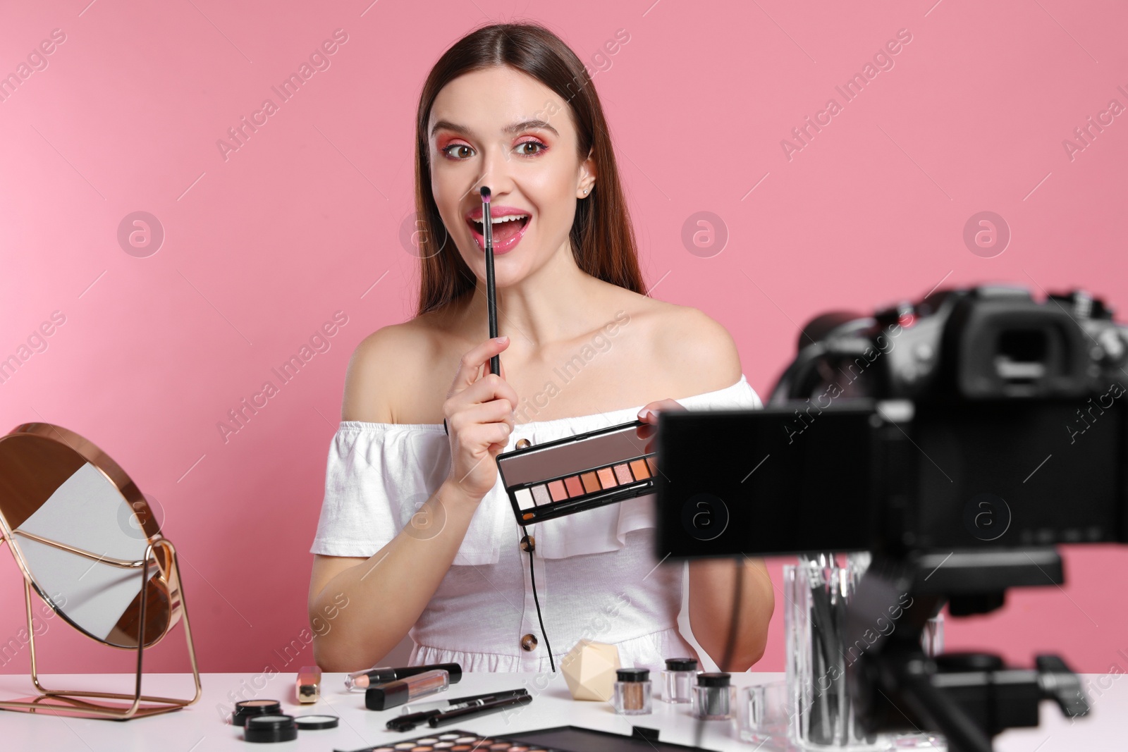 Photo of Beauty blogger recording makeup tutorial on pink background