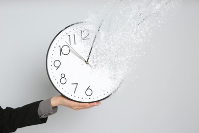 Image of Time is running out. Woman holding vanishing clock against light grey background, closeup