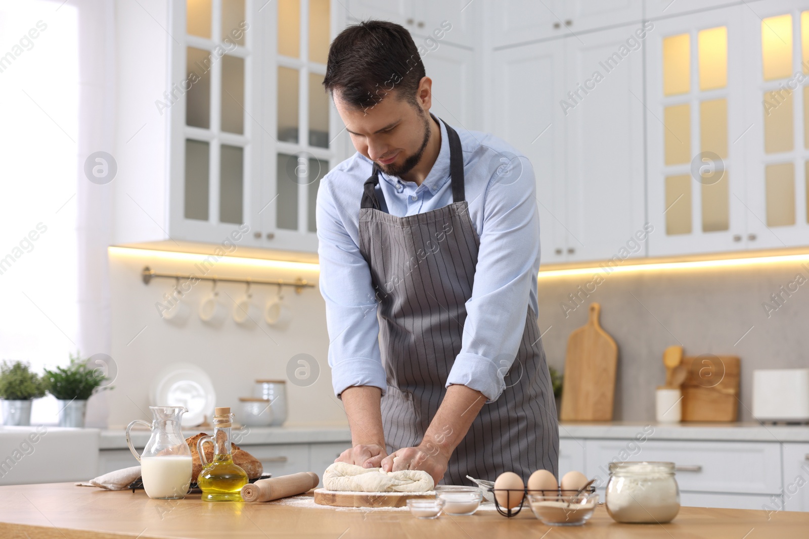 Photo of Making bread. Man kneading dough at wooden table in kitchen