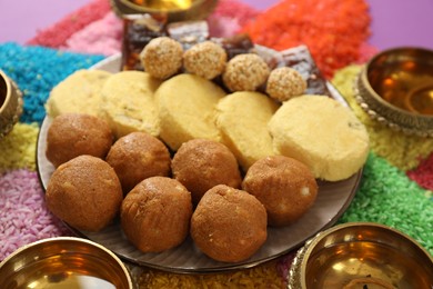Photo of Diwali celebration. Tasty Indian sweets, diya lamps and colorful rangoli on table, closeup
