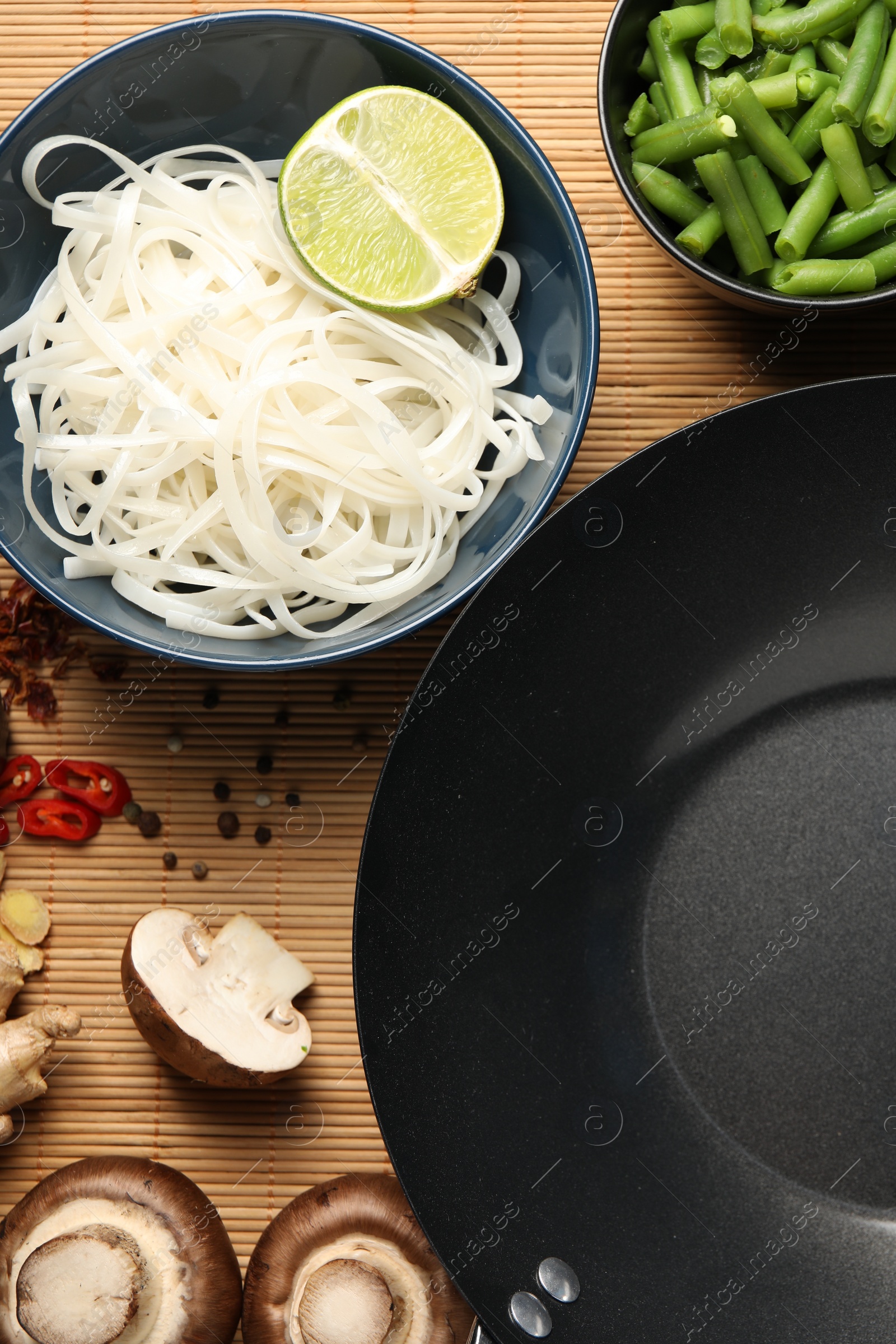 Photo of Flat lay composition with black wok, spices and products on bamboo mat