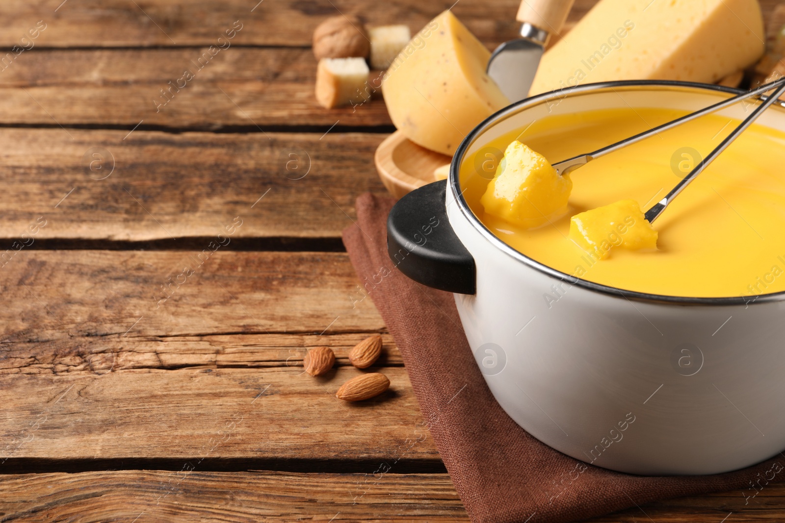 Photo of Pot of tasty cheese fondue and forks with bread pieces on wooden table. Space for text