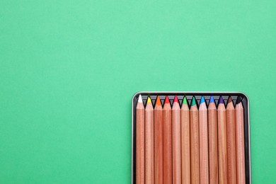 Photo of Box with many colorful pastel pencils on light green background, top view and space for text. Drawing supplies