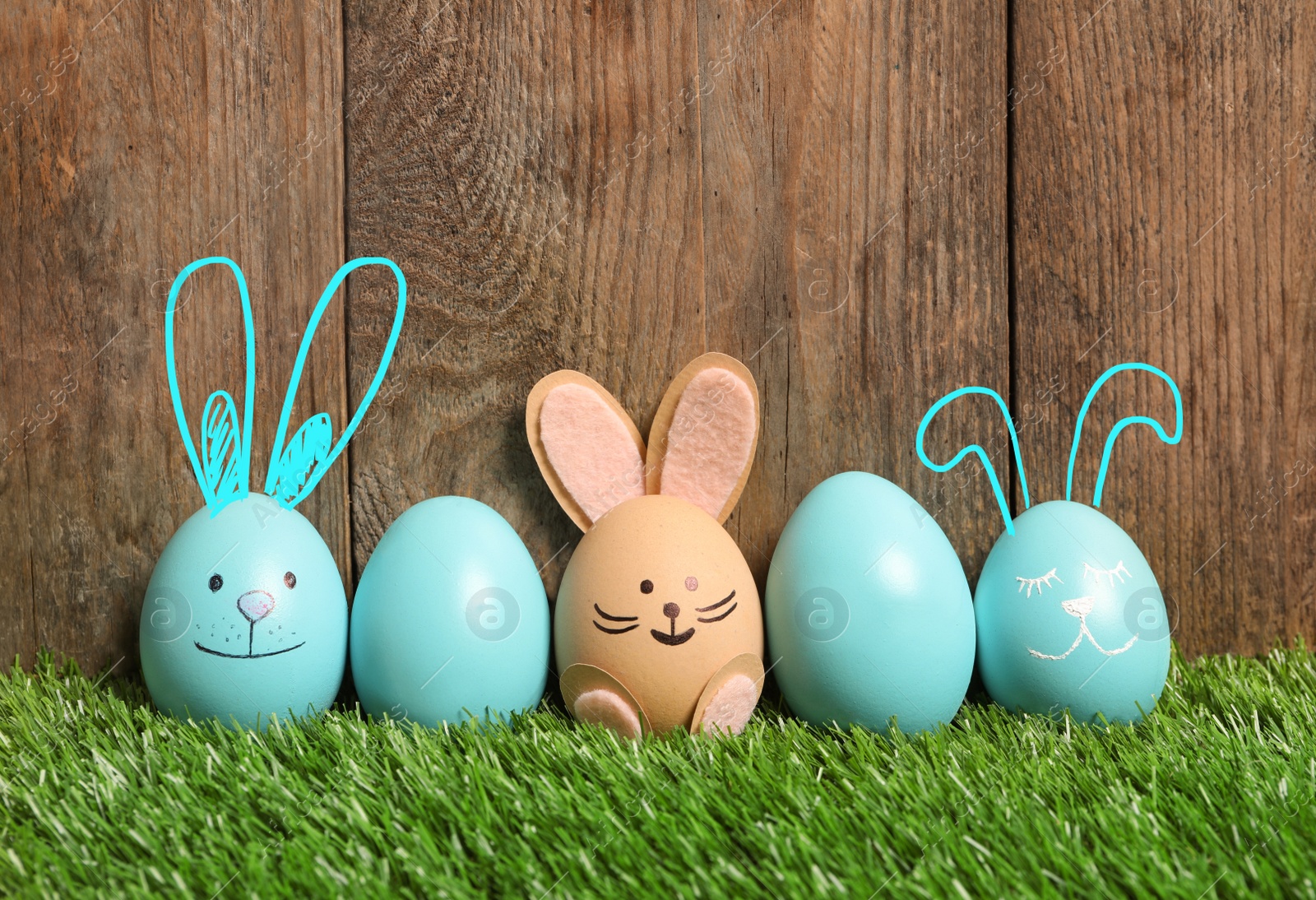 Image of Several eggs with ears as Easter bunnies among others on green grass against wooden background