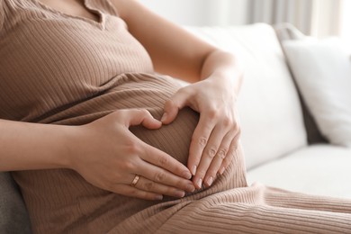 Photo of Pregnant young woman making heart with her hands on belly at home, closeup
