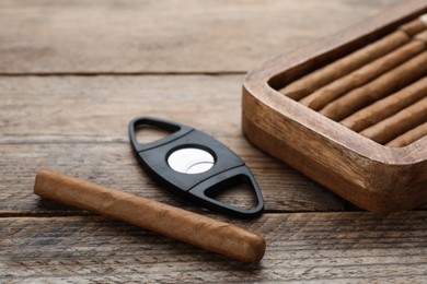 Photo of Cigars and guillotine cutter on wooden table, closeup