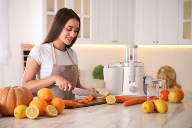 Photo of Young woman cutting fresh carrot for juice at table in kitchen
