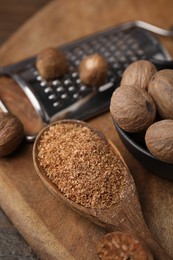 Spoon with grated nutmeg, seeds and grater on wooden table, closeup