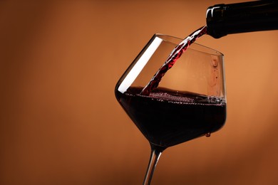 Pouring red wine into glass and bottles against brick wall background, closeup