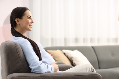 Photo of Happy pregnant woman on armchair at home, space for text