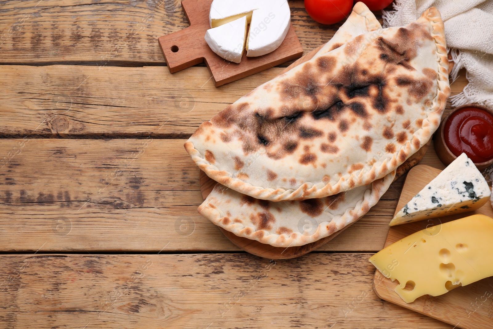 Photo of Delicious calzones and products on wooden table, flat lay. Space for text