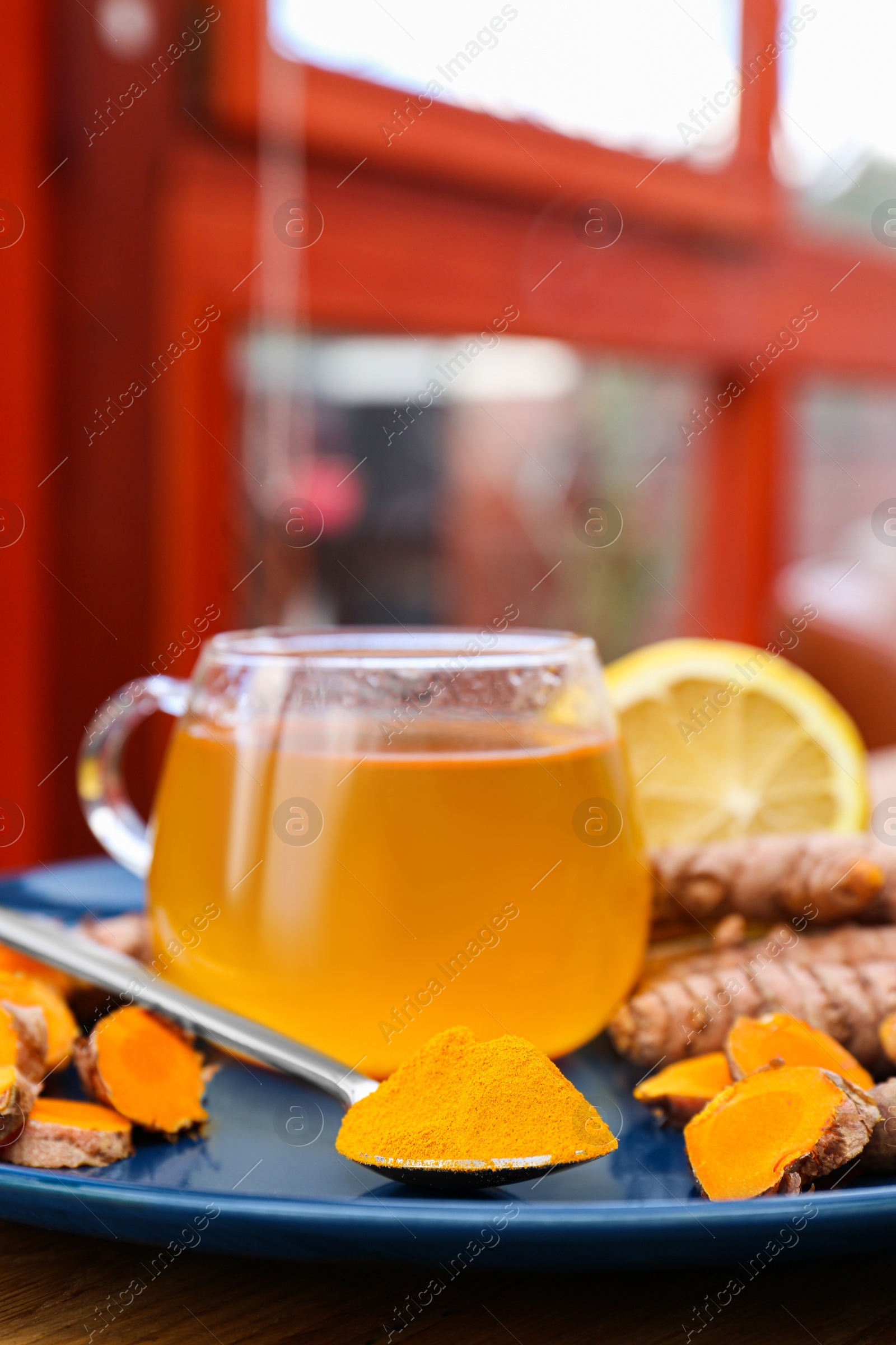 Photo of Plate with glass cup of hot tea, lemon, turmeric powder and roots on table