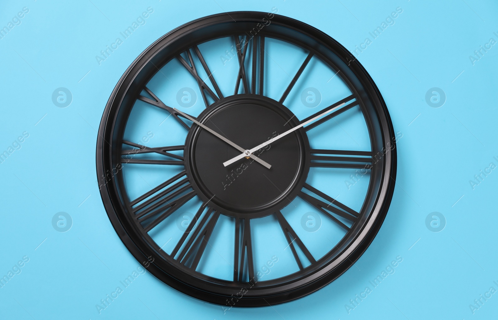 Photo of Stylish analog clock hanging on light blue wall