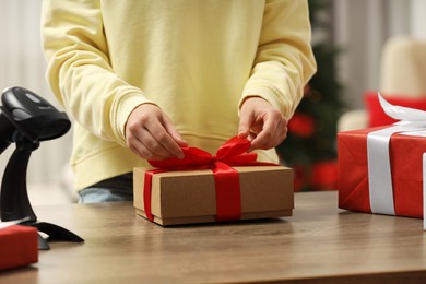 Photo of Woman preparing Christmas gift box at wooden table in post office, closeup