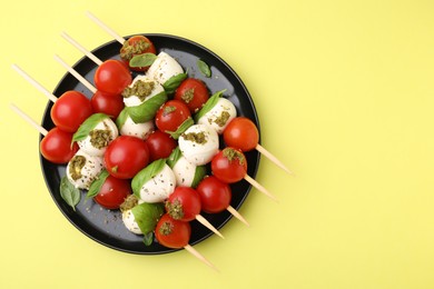 Caprese skewers with tomatoes, mozzarella balls, basil and pesto sauce on yellow background, top view. Space for text