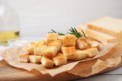 Delicious crispy croutons with rosemary on wooden board, closeup