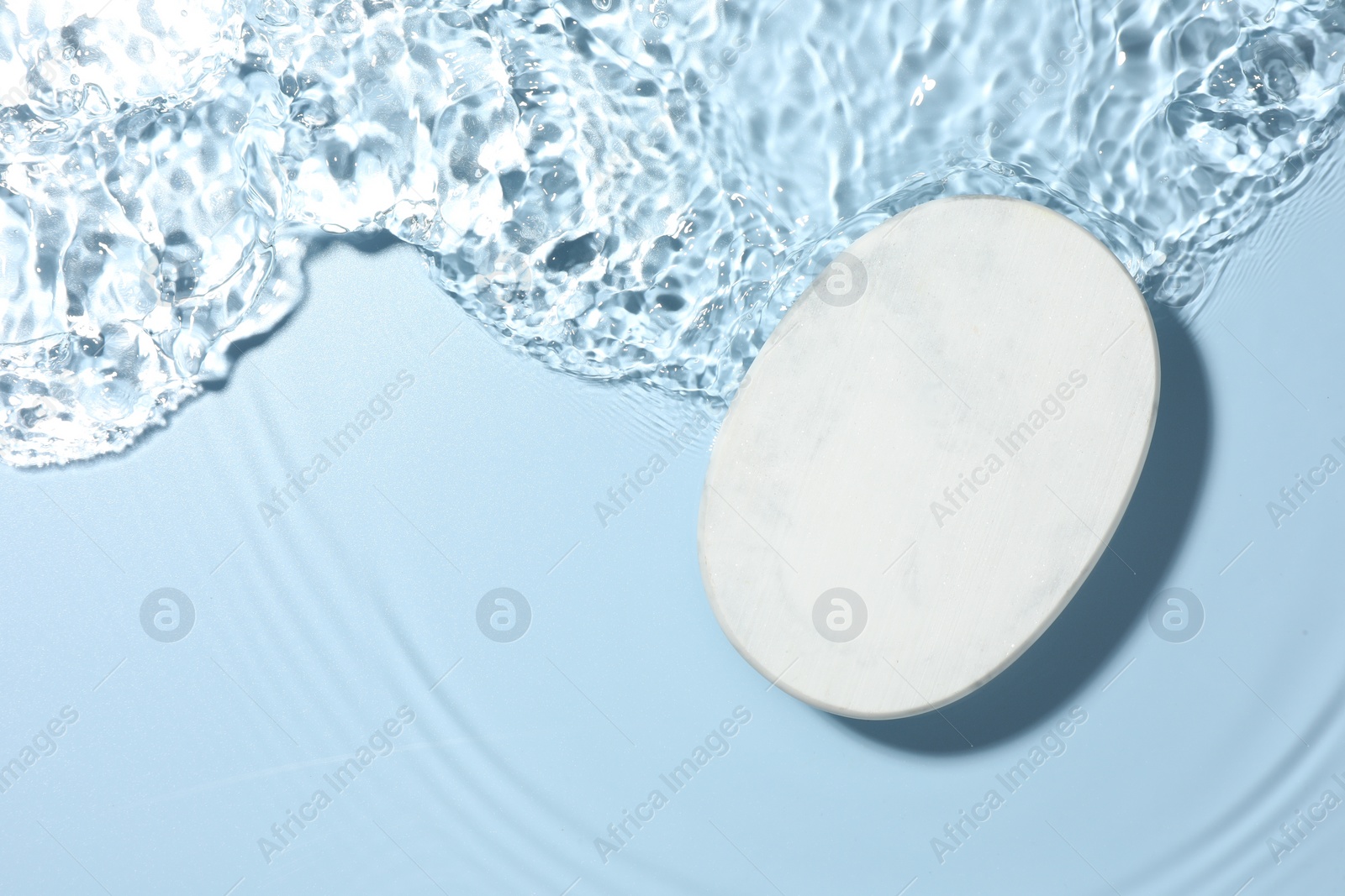 Photo of Presentation of product. White podium in water on light blue background, top view. Space for text