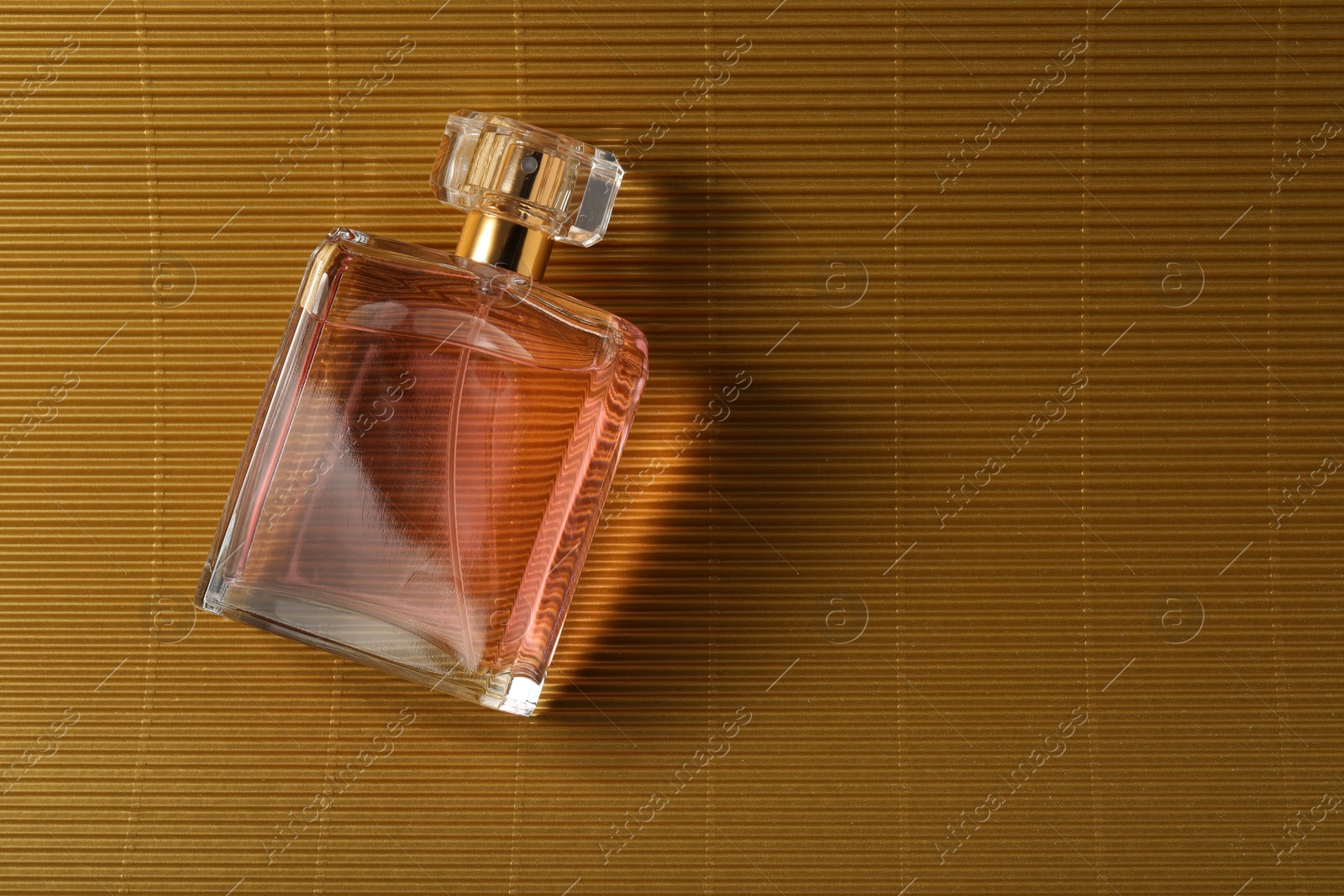 Photo of Luxury women's perfume. Sunlit glass bottle on golden surface, top view. Space for text