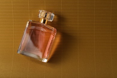 Photo of Luxury women's perfume. Sunlit glass bottle on golden surface, top view. Space for text