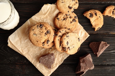 Flat lay composition with chocolate chip cookies and jar of milk on wooden background