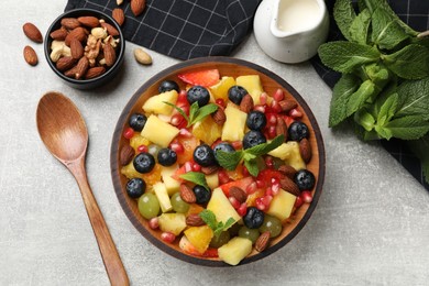 Photo of Delicious fruit salad in bowl, nuts and fresh mint on grey table, flat lay