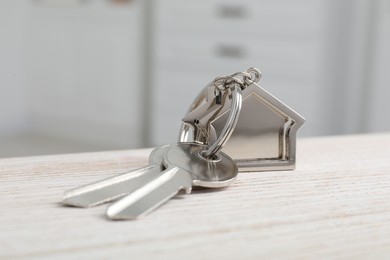 Keys with keychain in shape of house on wooden table against blurred background, closeup. Space for text