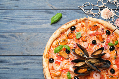 Photo of Tasty pizza with seafood and fresh basil on blue wooden table, flat lay