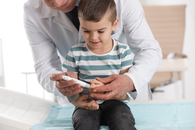 Photo of Little patient and doctor with lancet pen in hospital, closeup. Diabetes control